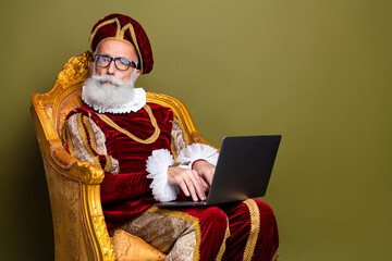 Elderly nobleman seated regally on a gilded chair using a laptop against a khaki green backdrop