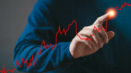 A person interacts with a digital graph, highlighting financial growth. Red line chart signifies market trends and analysis in a business setting.