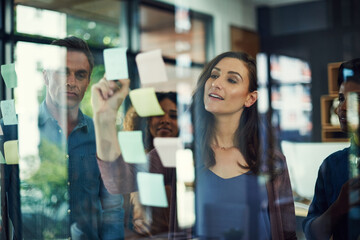 Sticky notes, storyboard and writing with business people in office together for brainstorming. Collaboration, meeting and training on glass with colleague group in workplace for strategy discussion