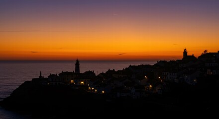 Dramatic sunset over coastal village with silhouetted lighthouse.