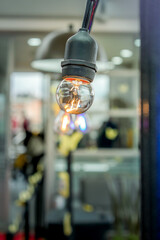 A glowing incandescent light bulb hanging from a black socket, with a blurred background of an urban setting, creating a warm and cozy ambiance.