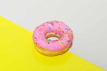Sweet strawberry glazed donut with sprinkles isolated on a half yellow and beige background,...