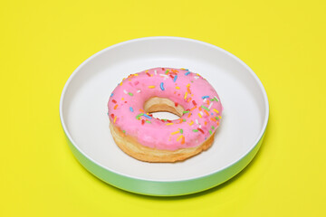 Sweet strawberry glazed donut with sprinkles in the plate. Isolated on yellow background, Delicious colorful donut. Cut out.