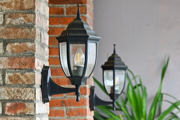 Photo of lamp light on the brick wall. Vintage iron lantern on the wall outdoor. Garden metal electrical lamp on the cafe or coffee shop. Wall lamp outdoor.