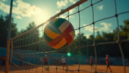 A volleyball stuck in a volleyball net with players in the background on a sunny day.