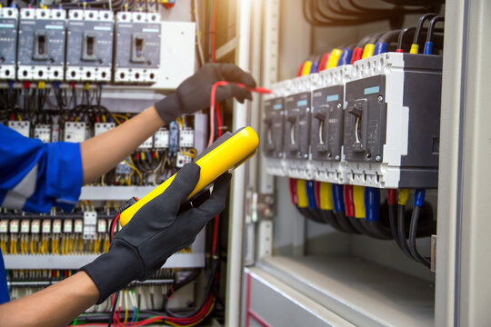 Electrical service technician holding electricity checking equipment to check electric current circuit breaker terminal panel and cable wiring main power distribution board for maintenance system.