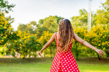 Young Woman in Retro Red Polka Dot Dress Wearing Headphones Listening and Enjoying Music in a Park...