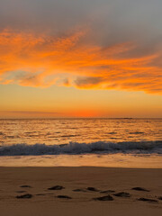 Obraz premium A breathtaking sunset over a serene beach, with vibrant orange and pink hues painting the sky. Gentle ocean waves roll onto the shore, leaving footprints in the golden sand.