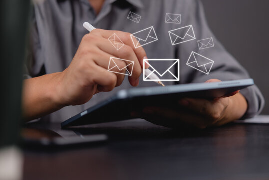 Businessman using a stylus on a tablet with floating email icons, representing digital communication, newsletter online messaging, and email marketing information in modern business solutions.