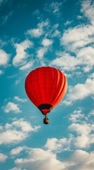 Naklejka premium Vibrant red hot air balloon floats gracefully in a blue sky with fluffy clouds.
