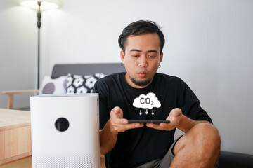 Pretty man sitting near air purifier and moisturizer appliance near sofa monitoring air quality in...
