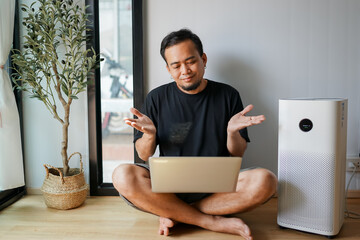 Air purifier in a living room, man working with laptop with filter for clean room 
