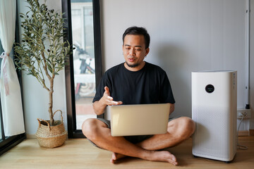 Air purifier in a living room, man working with laptop with filter for clean room 
