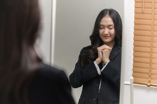 Young beautiful Asian woman in formal suit checking dressing tidiness and encourage herself in mirror at home before go for job interview. Woman recruitment employee or staff in company concept.