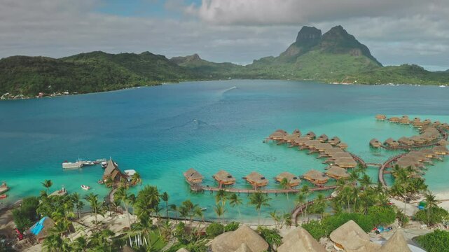 Luxury resort with wooden huts in Bora Bora, Mount Otemanu dominates the landscape behind turquoise lagoon. Visit French Polynesia. Exotic travel vacation getaway, romantic honeymoon. Aerial panorama
