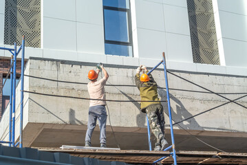 Workers standing on scaffolding work with hand-held power tools. Facade work at a height. Builders...