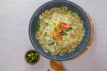 Steaming Bowl Of Egg Noodle Soup With Fresh Vegetables, Fluffy Egg, And Crispy Fried Shallots Served With Sliced Green Chilies For Extra Heat.