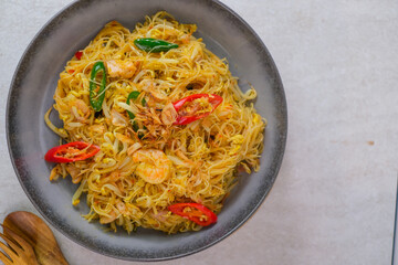 Savory Stir-Fried Vermicelli Noodles With Shrimp, Red And Green Chilies, Bean Sprouts, And Crispy Fried Shallots Served Fresh And Hot In A Grey Bowl.