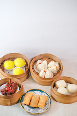 Assorted Dimsum Selection In Bamboo Steamers Featuring Custard Buns, Steamed Bao, Fried Spring Rolls, And Braised Chicken Feet On White Background.