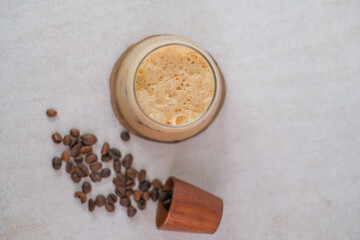 Top View Of Iced Coffee In Short Glass On Wooden Coaster With Spilled Roasted Coffee Beans From Wooden Cup On Light Textured Surface.