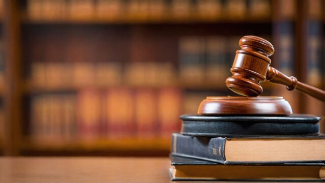 Wooden gavel rests on stack of law books on table. Legal framework update concept. Modern challenges require policy updates, new legal measures. Books signify updated legal provisions.