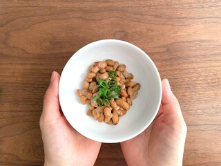 机上で納豆が入った皿を持つ女性の手元
