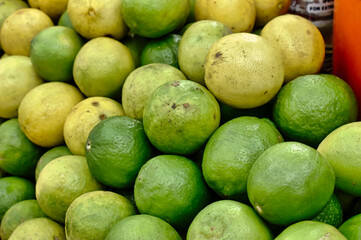 Limes and lemons are piled high at a bustling market, showcasing their fresh, vibrant colors against a bright backdrop
