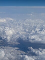 Fototapeta premium Aerial view of a snow-covered mountainous landscape partially obscured by thick, fluffy clouds. The sky above is a gradient of blue, contrasting with the white and shadowed areas of the clouds.