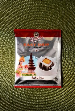 Jakarta, Indonesia - February 20th, 2025 - Kapal Api easy drip bali blend instant coffee sachet. Kopi saring praktis. Grounded coffee product packaging isolated on vertical green place mat background.