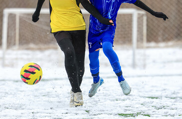Two young football soccer players in a competitive match on a snow-covered field, showcasing...