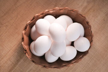 Fresh white eggs in a woven basket on wooden surface