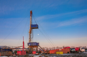Fototapeta premium Industrial winter landscape featuring an operational drilling rig with support facilities at a remote worksite during daylight hours