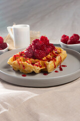 A golden waffle topped with fresh raspberries and raspberry sauce drizzling over it. The crispy texture and the glossy syrup, highlighting the vibrant colors of the dessert.