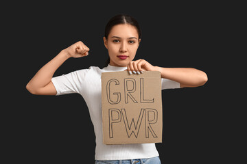 Young woman with sign GRL PWR flexing muscles on black background. Feminism concept
