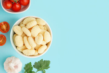 Bowl with tasty gnocchi, garlic and tomatoes on blue background