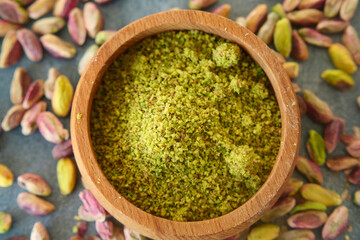 Ground pistachio nuts in wooden bowl surrounded by whole nuts