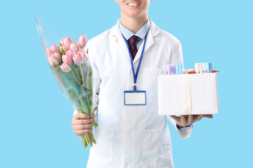 Male dentist with tulips and gift box on blue background. International Women's Day celebration