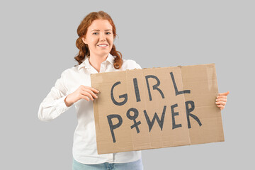 Beautiful young happy woman holding paper with text GIRL POWER on grey background. Women history...