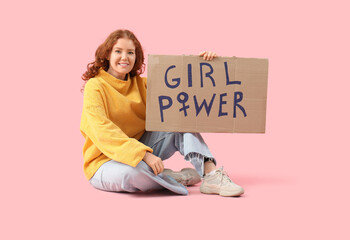 Beautiful young happy woman holding paper with text GIRL POWER and sitting on pink background....