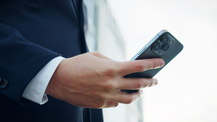 Businessman is typing text messages on mobile phone sitting in the park. Close up Male hands with smartphone, outdoors.  Human holds cell phone close up. Man holds mobile phone. Connection concept.