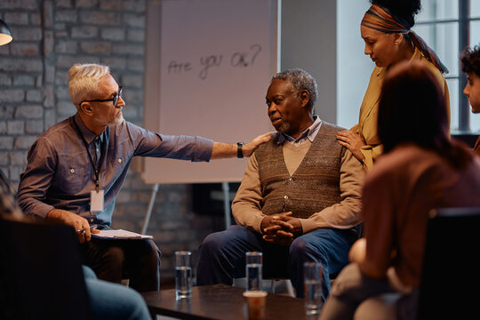 Black senior man receiving support from attenders of group therapy at mental health center.