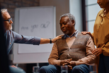 Sad black man being encouraged to talk about his issues during group therapy at community center.