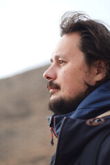A thoughtful man gazes into the distance, showcasing a rugged landscape behind him. His facial...