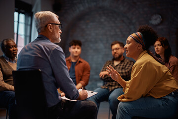 Mature woman communicating with mental health counselor during group therapy at community center.