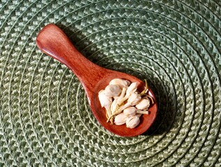 Organic dry jasmine flower buds on small wooden spice spoon object isolated on horizontal circular green fabric place mat background from top angle view.