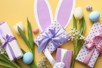 Easter eggs with gift boxes, flowers and paper bunny ears on orange background