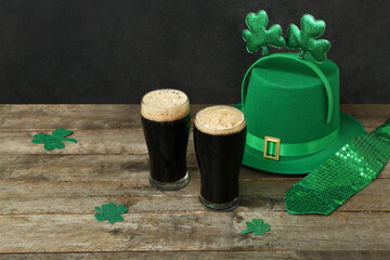 Glasses of dark beer with leprechaun hat, tie and decor for St. Patrick's Day celebration on wooden...