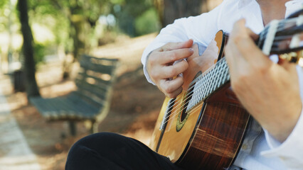 Man guitarist plays guitar outdoors. Musician plays a classical guitar in the park. A man in a white shirt plays a musical instrument outside the house. The guitarist plays the guitar.