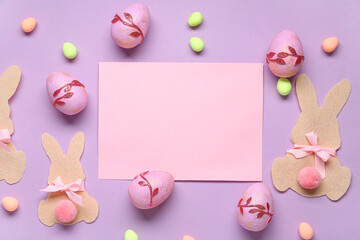 Paper Easter bunnies, painted eggs and blank greeting card on lilac background. Top view