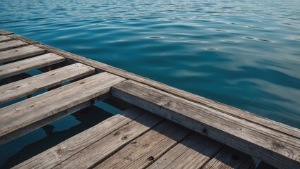 Fototapeta premium Serene view of a weathered wooden dock extending over calm blue lake water on a sunny day reflecting tranquility and natural beauty.